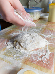 Hand sprinkles flour on piece of dough on table