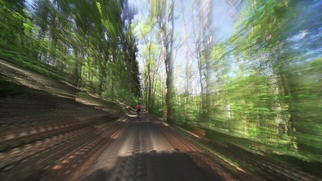 A solo female cyclist riding on the narrow forest road through the natural reserve of the Divoka Sarka in Prague.