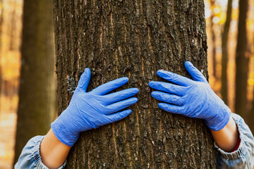 Hands in rubber gloves hug tree trunk