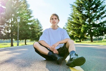 Fashion portrait of hipster teenager guy sitting on the road.