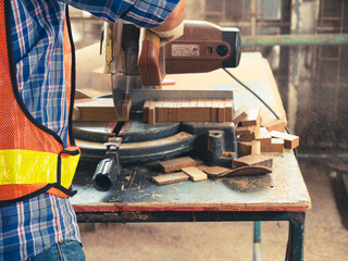 The carpenter craftsman wearing safety gear working with hardwood using a miter saw to cut a piece of wood in the workshop. Manufacture of wood products..