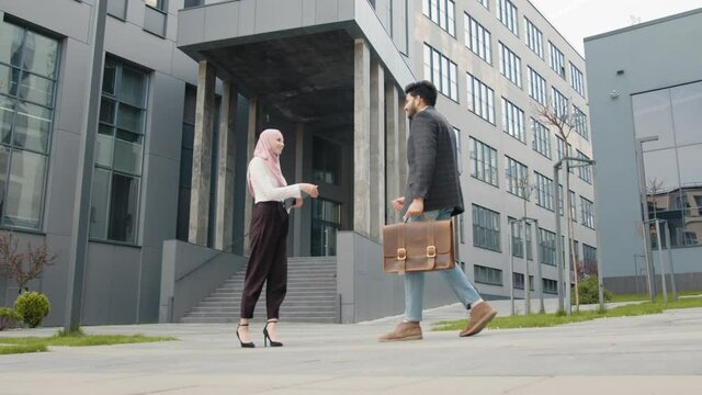 Side view of muslim business partners in formal clothes standing on street and shaking hands. Deal concept. Business partners shaking hands. Businessmen greet a muslim woman. Near the Modern Office