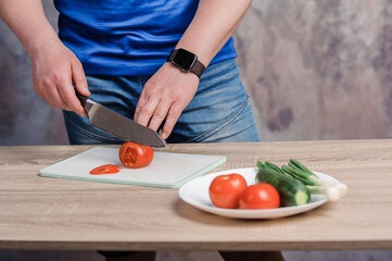 A man cuts a red tomato on a board. Cucumbers and tomatoes in a white plate