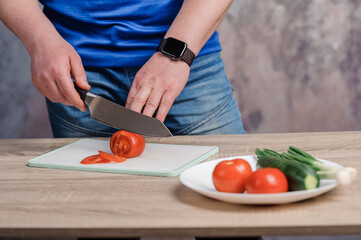 A man cuts a red tomato on a board. Cucumbers and tomatoes in a white plate
