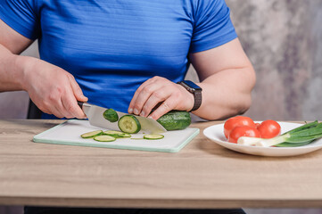 A man cuts a cucumber on a board. Tomato and green onions lie on a white plate