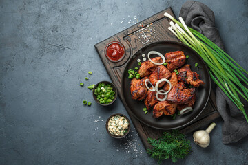 Fried meat with onions, sauces and fresh herbs on a dark gray-blue background. Kebab, barbecue.