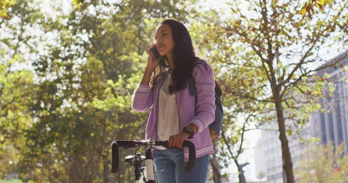 Asian woman with bicycle smiling talking on smartphone while standing in the park