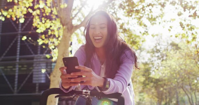 Asian woman with bicycle smiling while using smartphone in the park