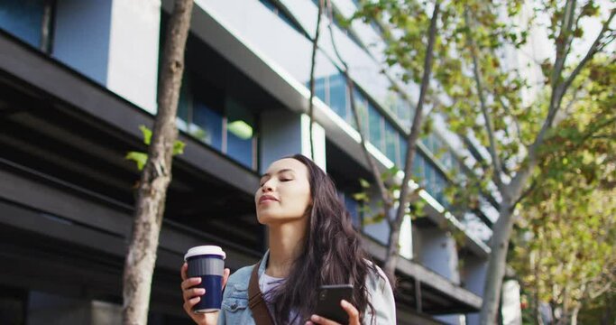 Asian woman walking using smartphone and drinking takeaway coffee