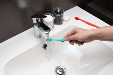Hand holding toothbrush under flowing water from the faucet. Oral Care and Hygiene. Dental health. Morning concept.