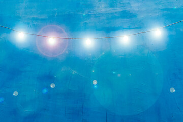Bright garland of glowing light bulbs with highlights on background of blue plaster wall. Festive blue background for a postcard with highlights. Outdoor string lights hanging on line on wall house.