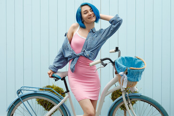 Fototapeta na wymiar Cute girl on a white bike with busket on blue wall. South side near sea.