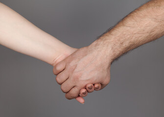 Hands of man and woman holding together, Gray background.