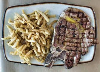 Chuletón de ternera a la parrilla con un chorro de aceite de oliva y patatas naturales fritas
