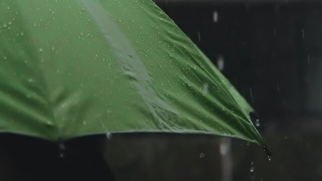  Slow motion shot of rain drops on green umbrella on dark background
