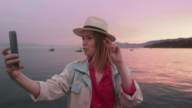 Portrait of happy woman making selfie picture on smartphone camera, pink sunset 