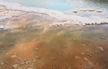 Sand covered with crystalline salt on shore of Dead Sea, clear calm water near - typical scenery at Ein Bokek beach, Israel