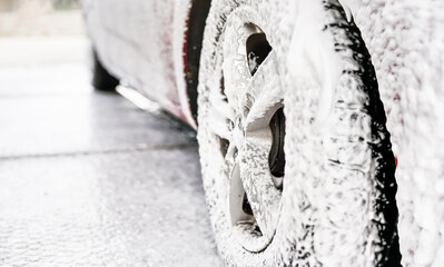 Detail on car wheel covered with lot of soap and shampoo foam, when being washed in carwash