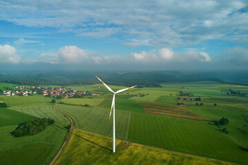 One wind turbine in the center of the picture on an agricultural field. Narrow road leading to a village on the swabian alb in germany. Blue sky with storm-like clouds. Aerial view.