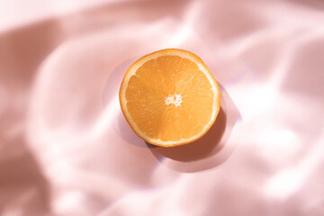 Fresh orange fruit on a pastel pink background with liquid water shadow