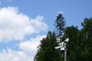 Cctv camera attached on a metal pole with coniferous trees and sky on the background and a lot of copy space. It serves for protection of property for both private persons and copamanies.