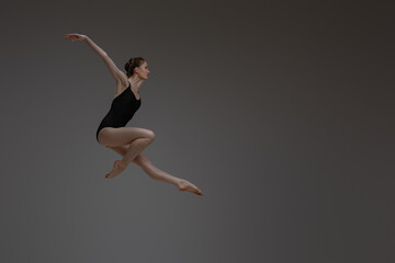 Fototapeta na wymiar Professional leaping ballerina dancing against gray background