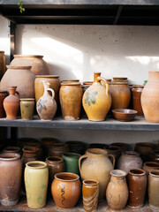 Fototapeta na wymiar Clay products. Brown yellow and color flower pots and vases in artisan workshop. Vertical photo. Ceramic brown pots and vases on shelves in a craftsman's studio. Handmade