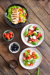 different salads vegetables, grilled chicken breast, olives, feta, tomato, onion, cucumber other on the table, healthy food