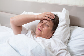 Fototapeta na wymiar Sick elderly woman on the bed. Grandma has a bad headache.
