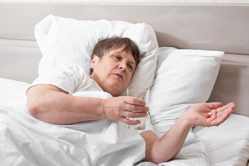Sick elderly woman on the bed. Grandma is about to take her pills.