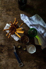 Glass of light beer on a dark brown table with snacks. Top View