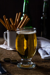 Glass of light beer on a dark brown table with snacks