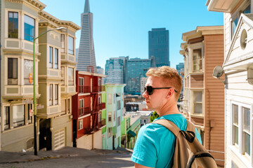 A young man walks along a beautiful street with a view of the Transamerica Tower in San Francisco