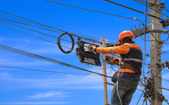 Low angle view of technician on wooden ladder is installing fiber optic system in internet splitter box on electric pole against blue sky background
