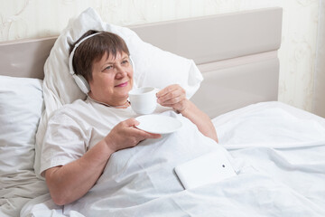 Morning coffee for grandma. An elderly woman with headphones listens to music and drinks coffee.