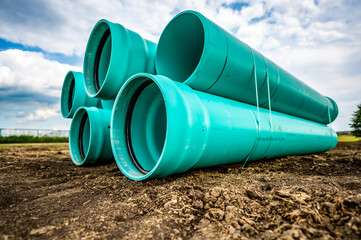 Stacked water main pipe with bell fitting next to an exposed trench for installation
