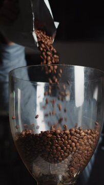 Close up of barista pours coffee beans into a coffee grinder from package in slow motion. Vertical video template for smartphone web promo.