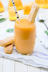 Glass of fresh cantaloupe smoothie with cookies and birch staraw  on white wooden boards.