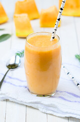 Glass of fresh cantaloupe smoothie with straw birch  on white wooden boards.