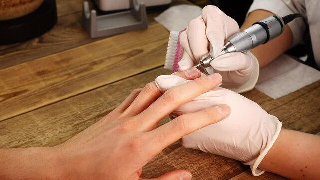 Closeup view of manicurist work who polishes clients nails and cuticles by electric drill. Female master in protective gloves uses special machine during beauty procedure. Concept of apparat manicure.