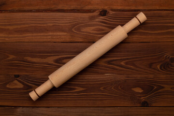 Traditional handmade organic wooden culinary dough rolling pin for cooking on a brown background with wooden texture. Kitchenware. Top view, Close Up