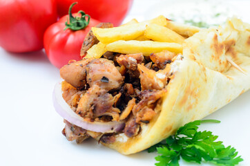 Plate of traditional Greek pita gyros with meat, fried potatoes, tomato and onion