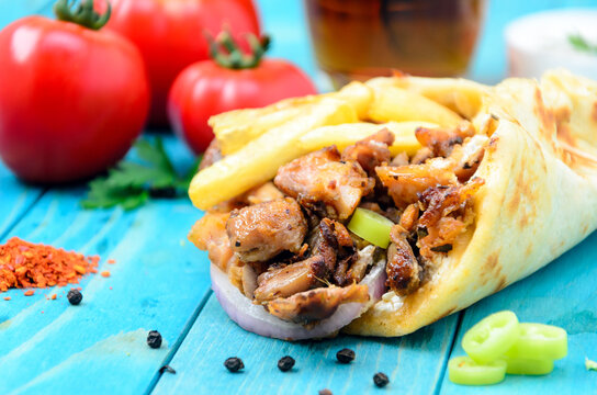 Plate of traditional Greek gyros with meat, fried potatoes, tomato and onion on light blue wooden table