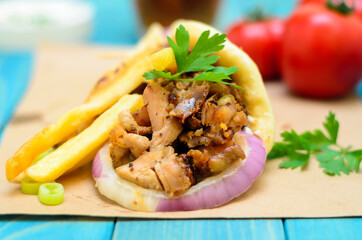 Traditiona Greek pita gyros with meat, fried potatoes, tomato, onion and drink on brown Paper, Placed on blue Wooden Table