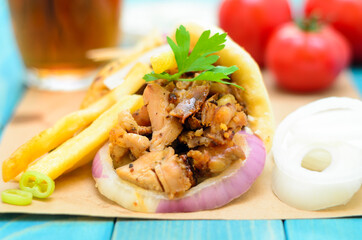 Traditiona Greek pita gyros with meat, fried potatoes, tomato, onion and drink on brown Paper, Placed on blue Wooden Table