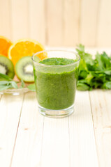 Healthy green smoothie with spinach, kiwi and orange in a glass on light wooden table