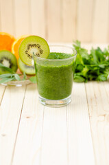 Healthy green smoothie with spinach, kiwi and orange in a glass on light wooden table