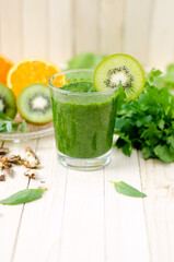 Healthy green smoothie with spinach, kiwi and orange in a glass on light wooden table