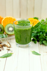 Fototapeta premium Healthy green smoothie with spinach, kiwi and orange in a glass on light wooden table