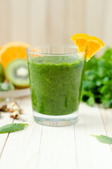 Healthy green smoothie with spinach, kiwi and orange in a glass on light wooden table
